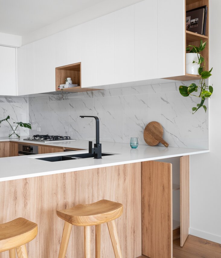 Bright kitchen with black elements, marble wall tiles and light wood facades