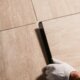 Two hands of a Ramsauer employee inserting and bonding a beige tile between other tiles.