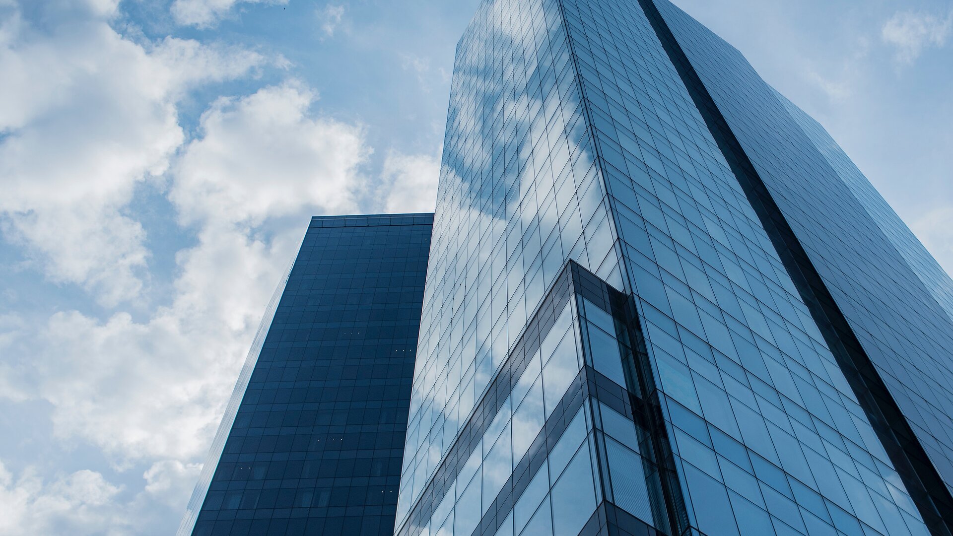 Hochhaus mit Glasfassade mit Blick von unten nach oben, bläulich gestimmtes Bild.