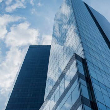 Hoog gebouw met glazen gevel van onderaf gezien, blauw getinte foto.