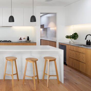 Modern white kitchen with wooden elements, white kitchen island and wooden stool.