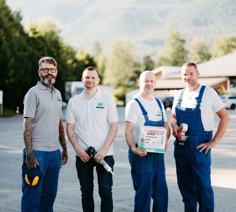 Four Ramsauer employees in work clothes with different tools. 